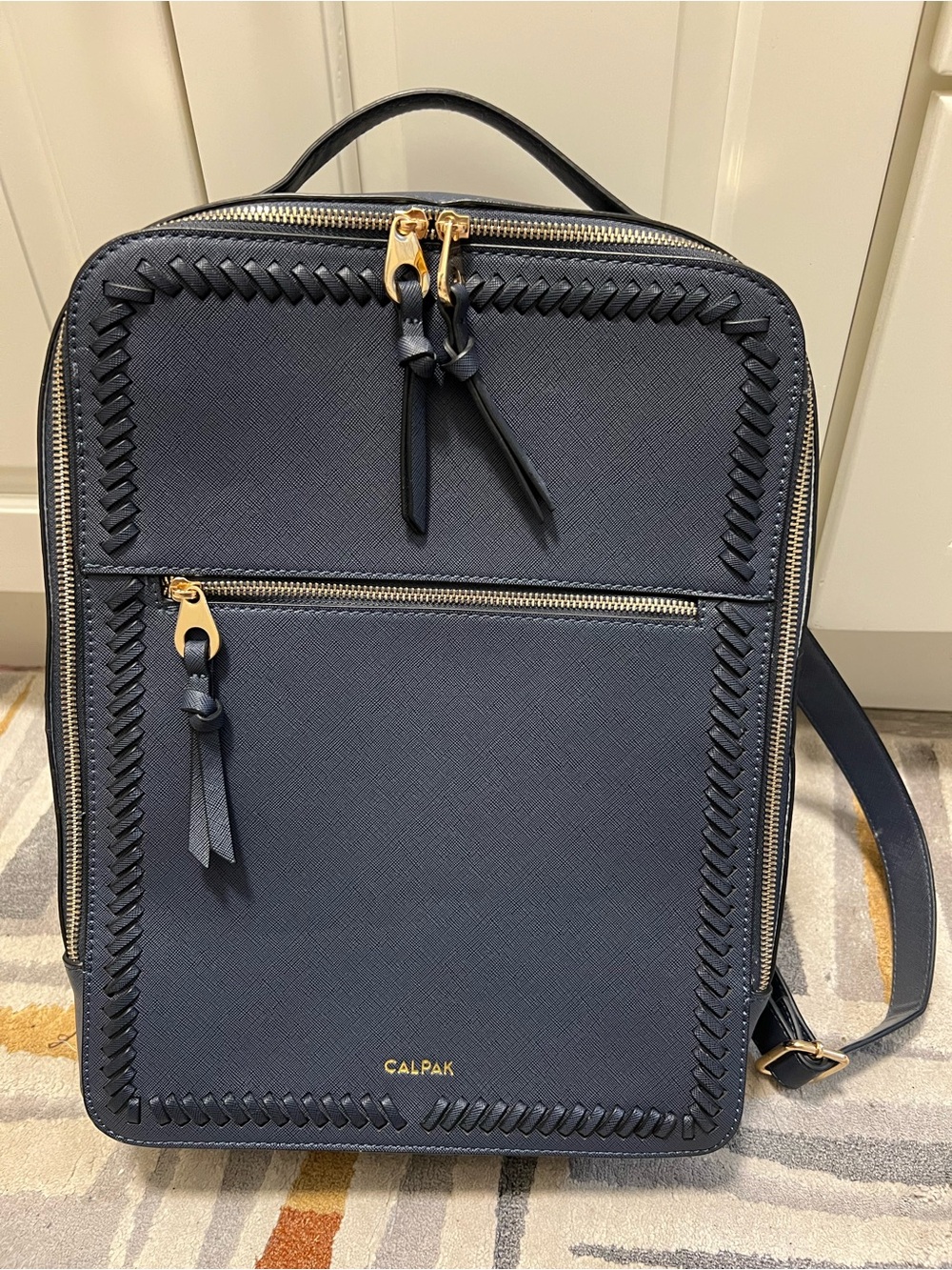 Calpak navy backpack with gold hardware and woven trim